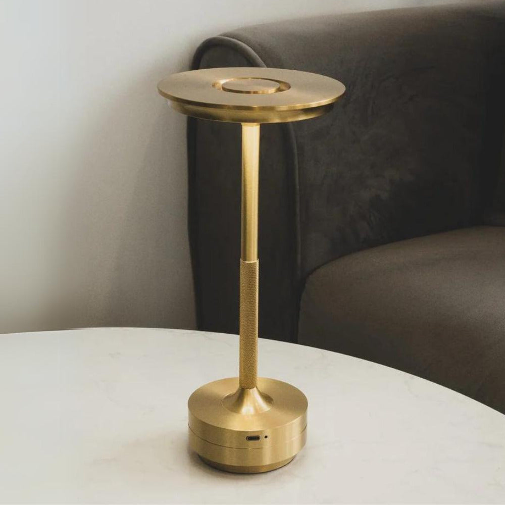 Elegant cordless brass table lamp placed on a side table next to a dark sofa, perfect for living rooms.