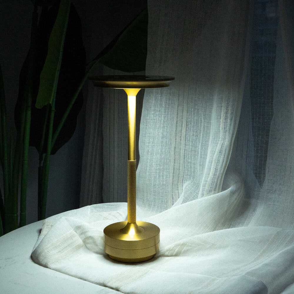 Brass cordless table lamp glowing softly next to white curtains, perfect for bedside lighting.