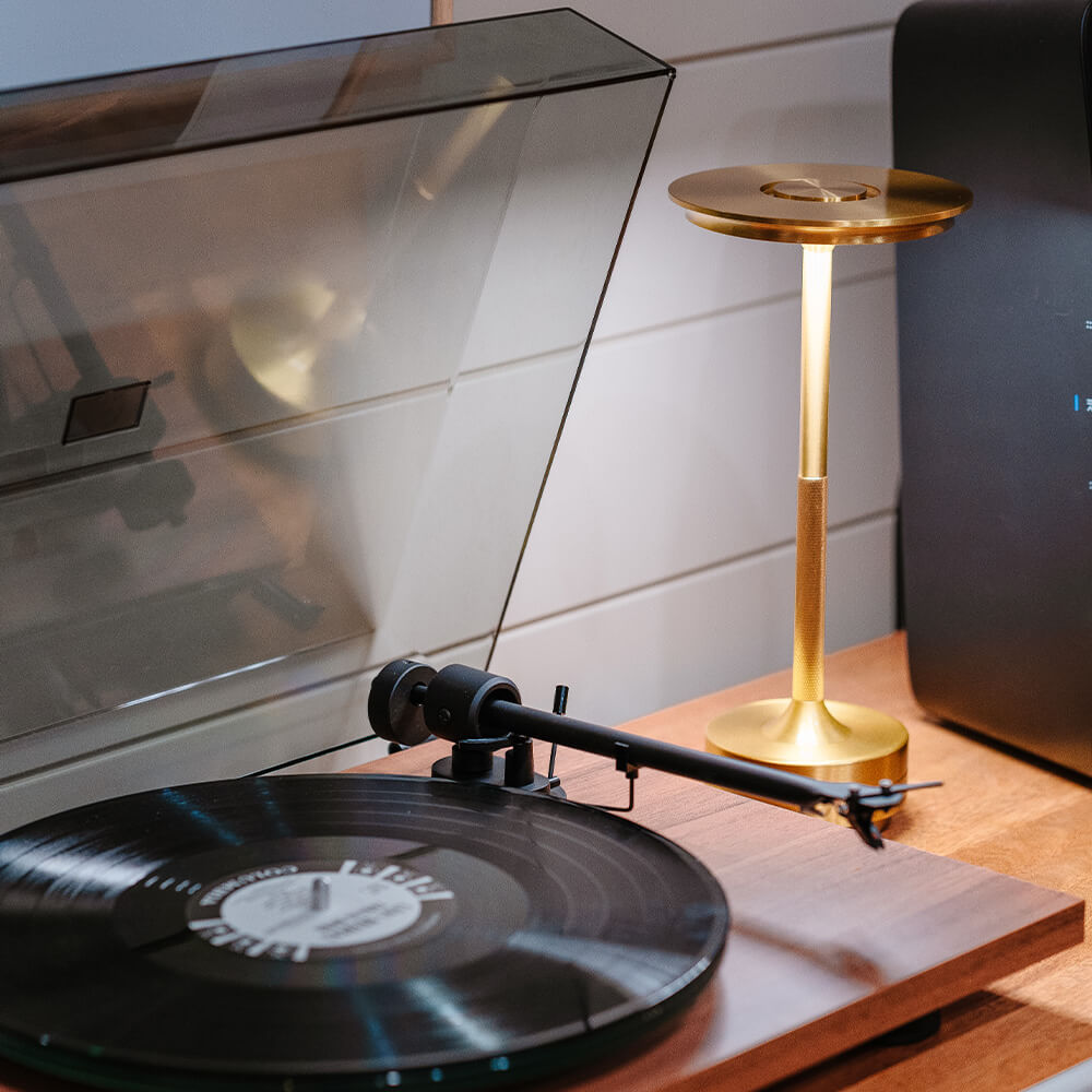 Gold cordless table lamp placed on a wooden surface next to a vinyl record player, ideal for a vintage setting.