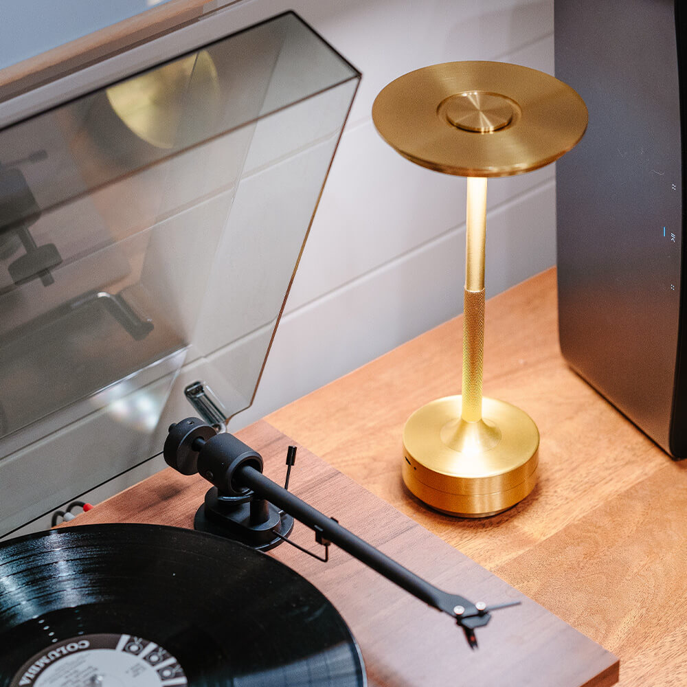 Elegant brass cordless table lamp on a desk beside a record player, perfect for a modern music corner.