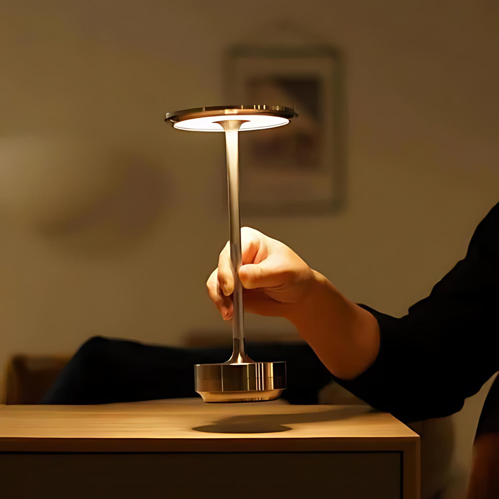 A hand holding a brass cordless table lamp with dimmable LED light, perfect for portable use.