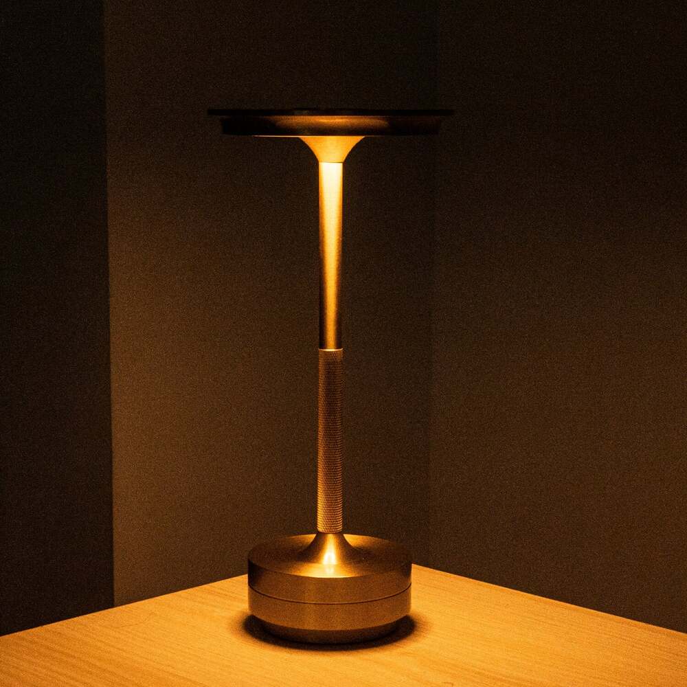 Gold cordless table lamp illuminating a wooden surface, ideal for ambient lighting in modern interiors.