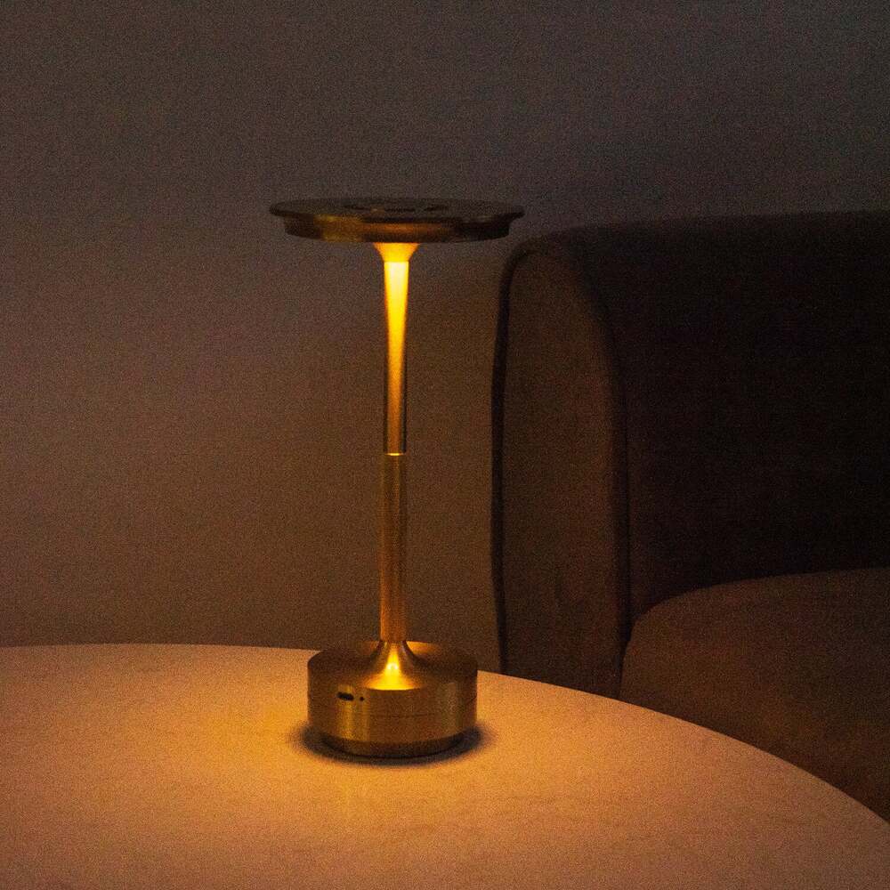 Brass cordless table lamp on a table beside a sofa, creating a cozy atmosphere with warm LED lighting.