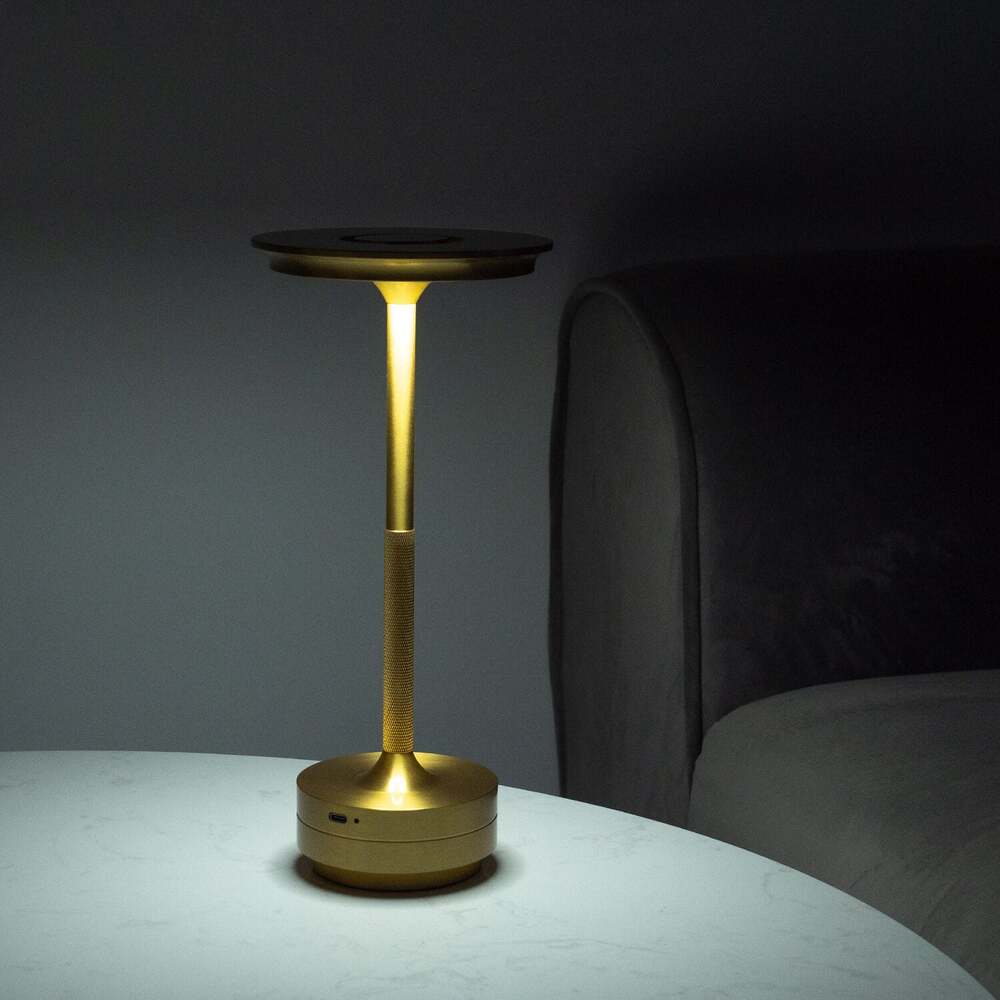 Elegant brass cordless table lamp glowing softly on a white table, suitable for night-time use.