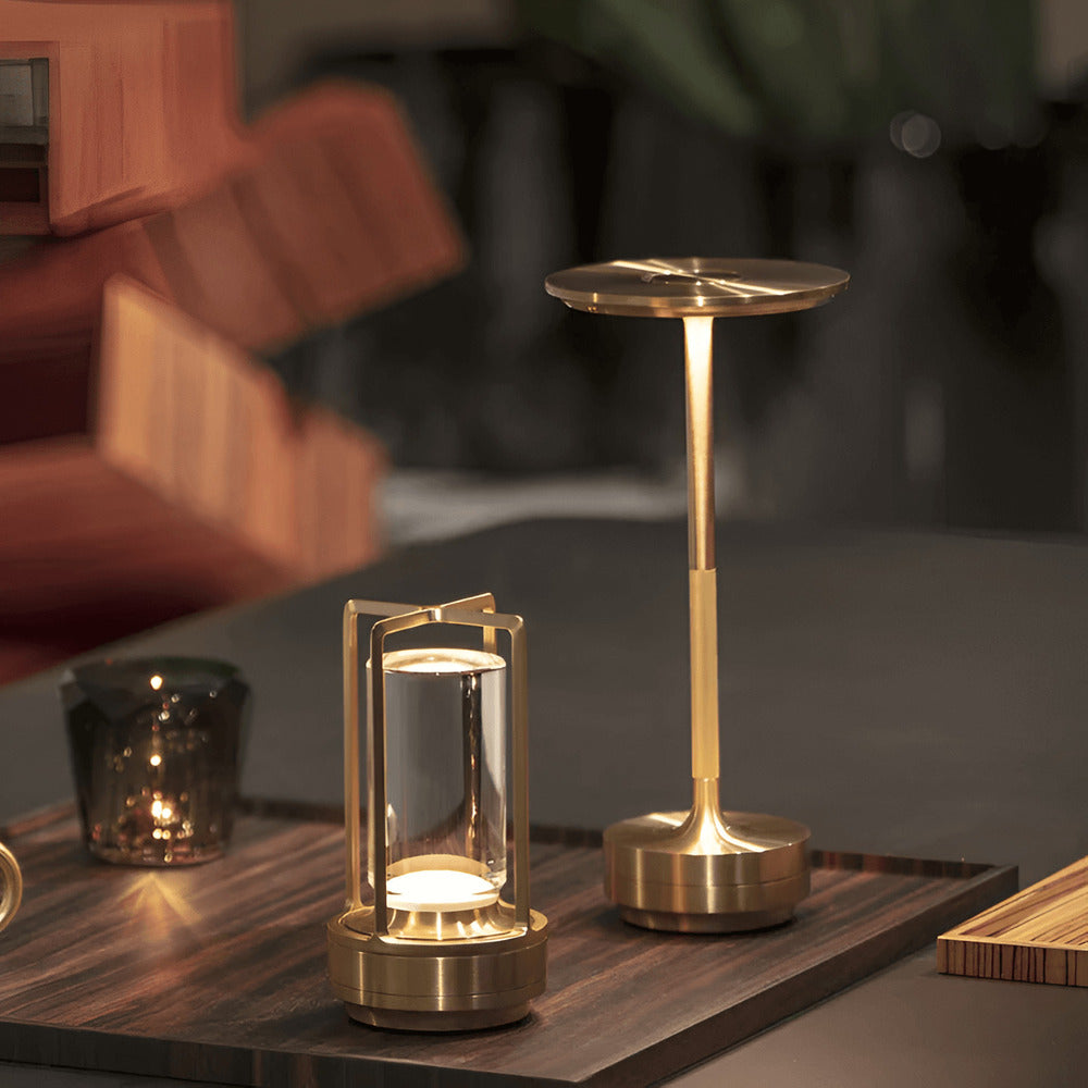 Brass cordless table lamp next to a decorative glass light on a wooden tray, perfect for elegant interiors.