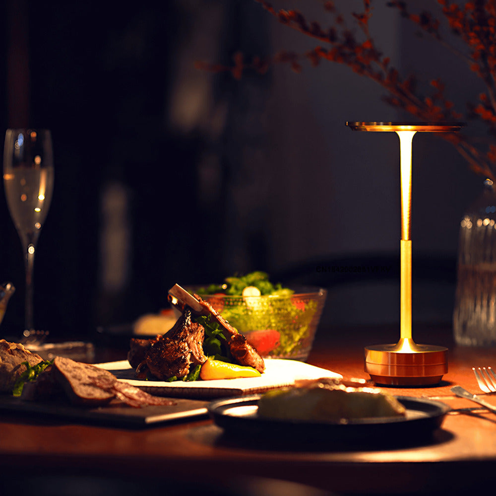 Brass cordless table lamp on a dining table, providing soft light for a cozy dinner setting.