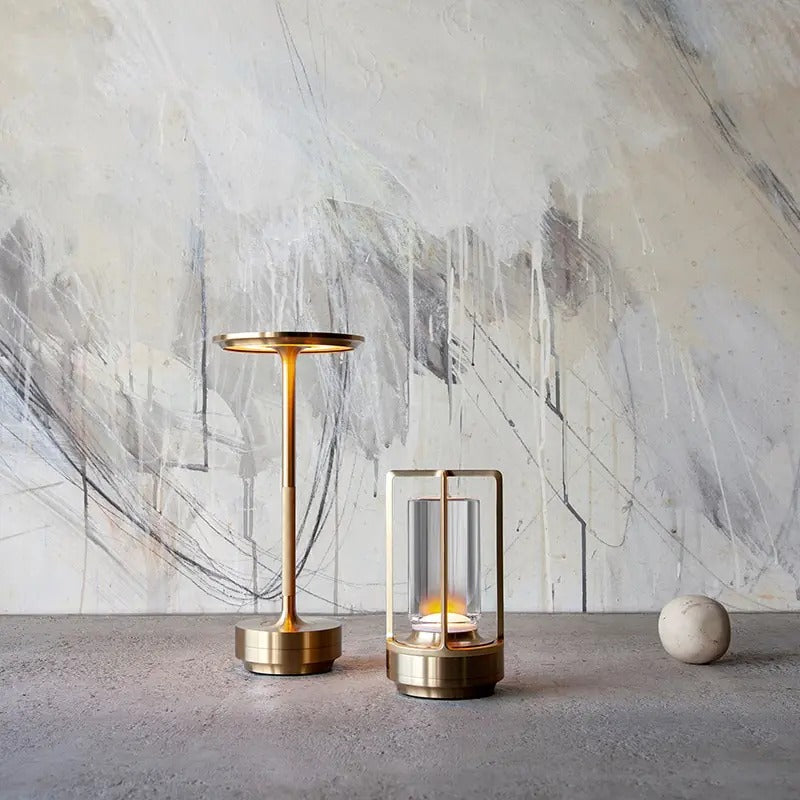 Brass cordless table lamp next to a decorative light, placed against a contemporary abstract wall.