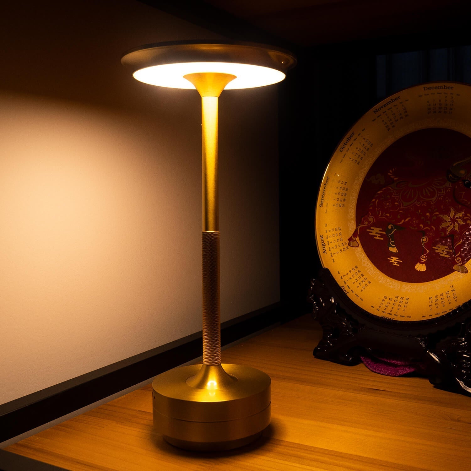 Gold cordless table lamp on a wooden shelf, providing warm light in a cozy room setting.