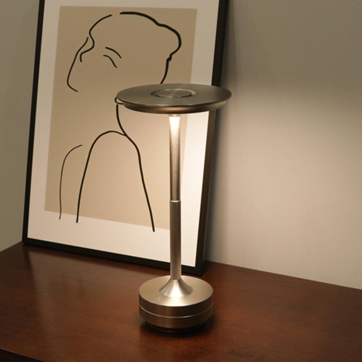 Minimalist portable table lamp in a silver metallic finish, placed on a wooden nightstand next to modern art decor, perfect for modern and contemporary interiors.