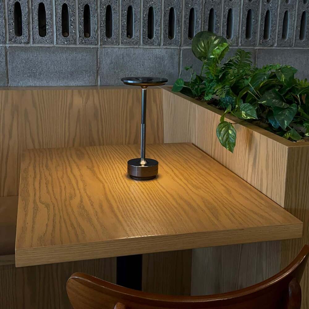 Portable cordless desk lamp in a modern restaurant booth with plants and wooden decor.