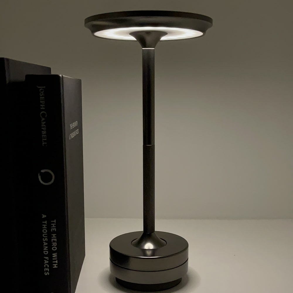 Cordless table lamp with a sleek, modern design, placed next to a book titled "The Hero with a Thousand Faces"