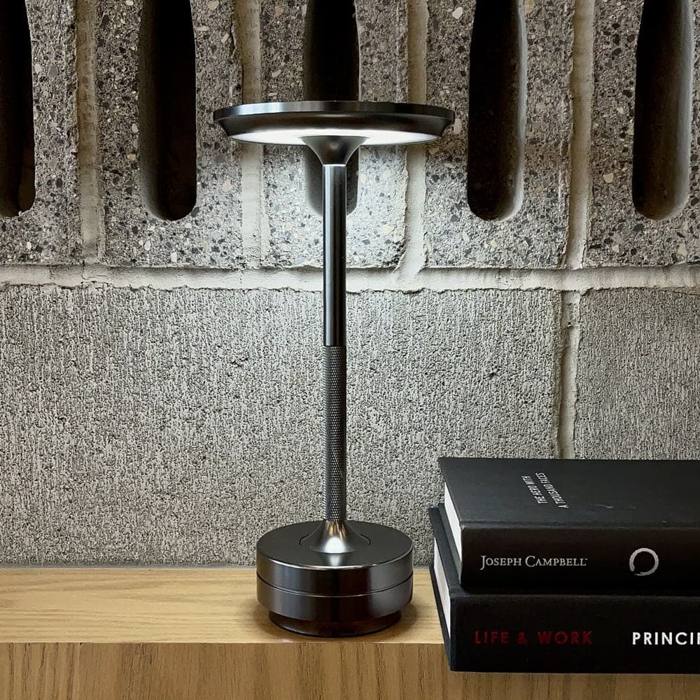 Cordless rechargeable table lamp on a wooden shelf with books, showcasing its sleek and modern design