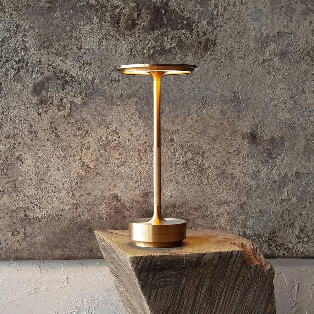 Gold cordless table lamp with sleek metal design placed on a wooden block.