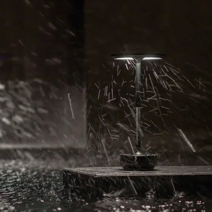 Water-resistant cordless table lamp in black, illuminated in heavy rain, ideal for outdoor use.