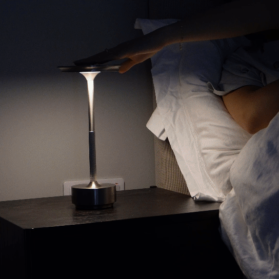 A person reaching to turn on a cordless table lamp on a bedside table, perfect for nightstand or reading.