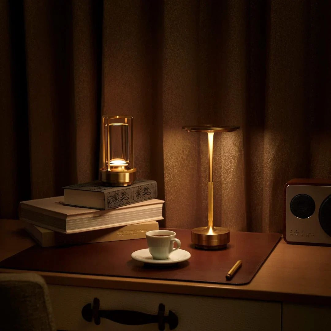 Cordless brass table lamp on a desk next to books and a cup, creating a cozy night-time setting.