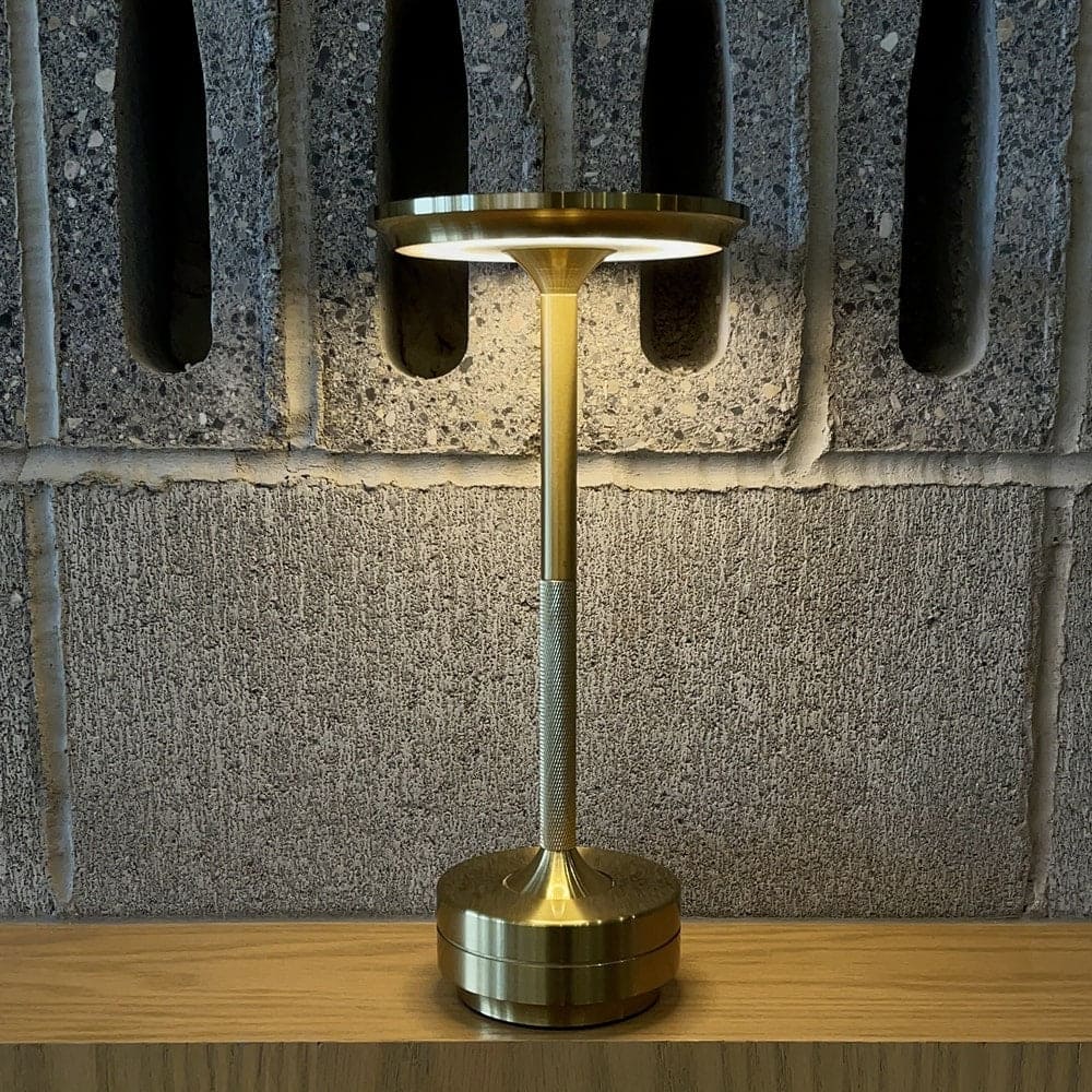 Brass cordless table lamp on a shelf against a concrete wall, ideal for industrial-style interiors.