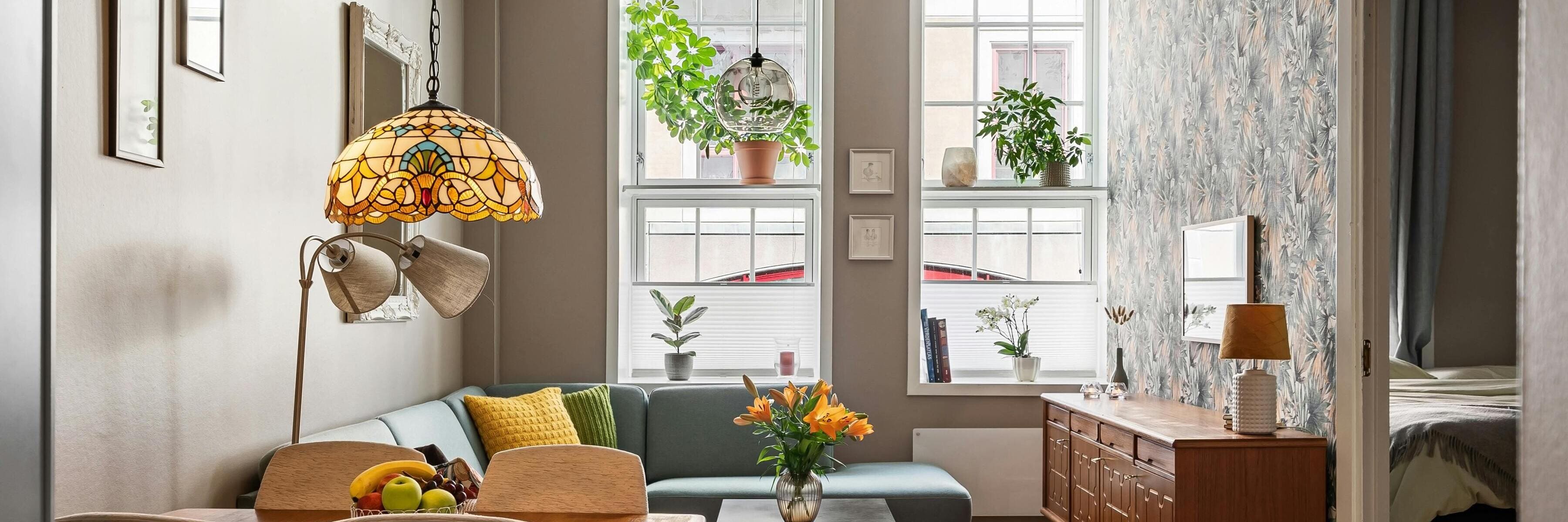 Living room with stained glass pendant, green sofa, wooden sideboard, and plants on windowsills. Mid-Century Modern and Classic style.