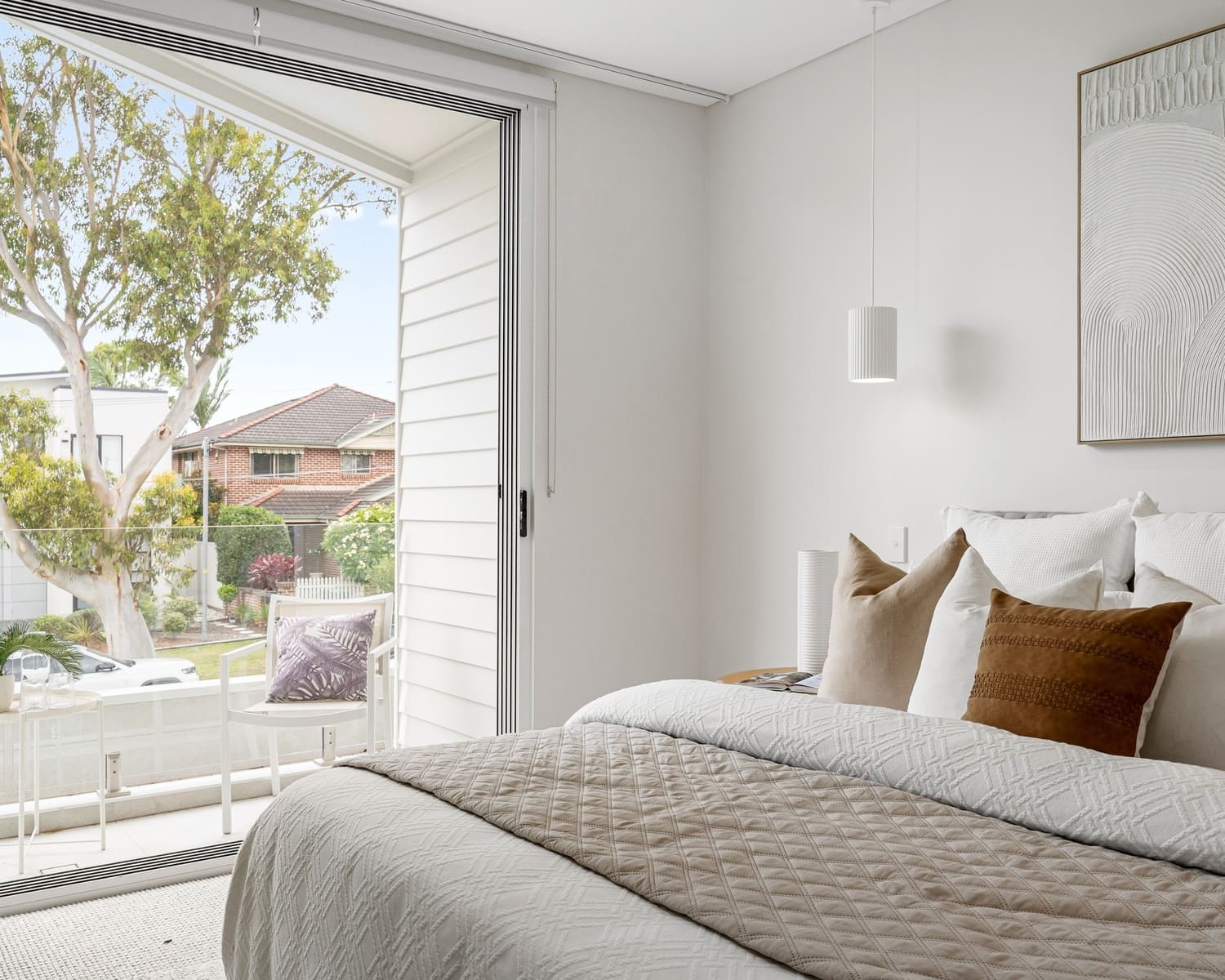 A serene bedroom setting with a modern pendant light hanging above the bedside, casting a soft glow over the bed and enhancing the calm, minimalist decor of the room.