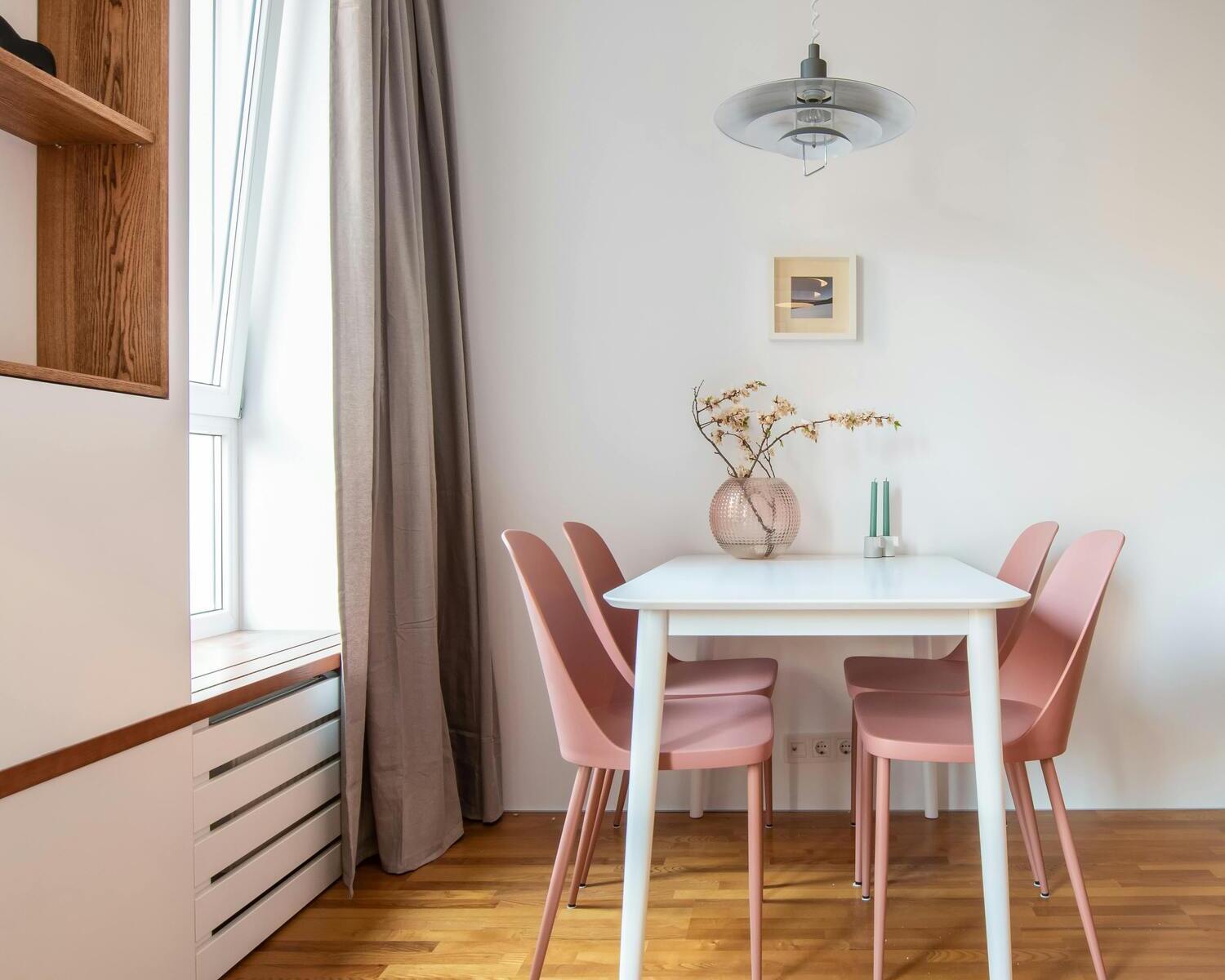 Contemporary small dining area with a white table, pink chairs, and a round metal pendant light hanging above, creating a cozy atmosphere.