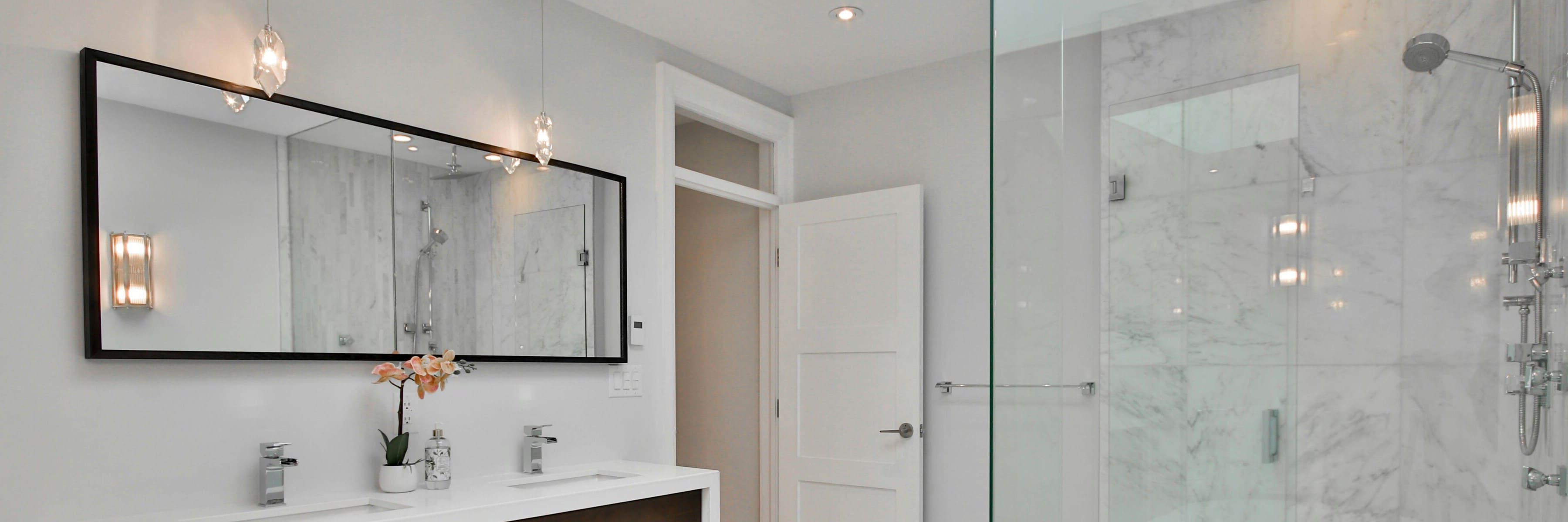 Modern bathroom lighting with pendant lights above a large mirror, featuring a white sink and wooden accents.