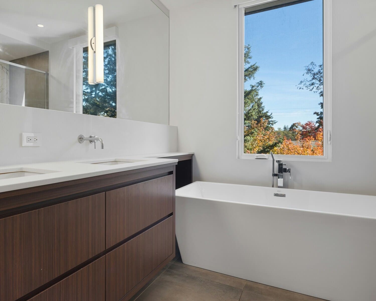 Bright bathroom with a large window, white bathtub, and modern lighting above the mirror.