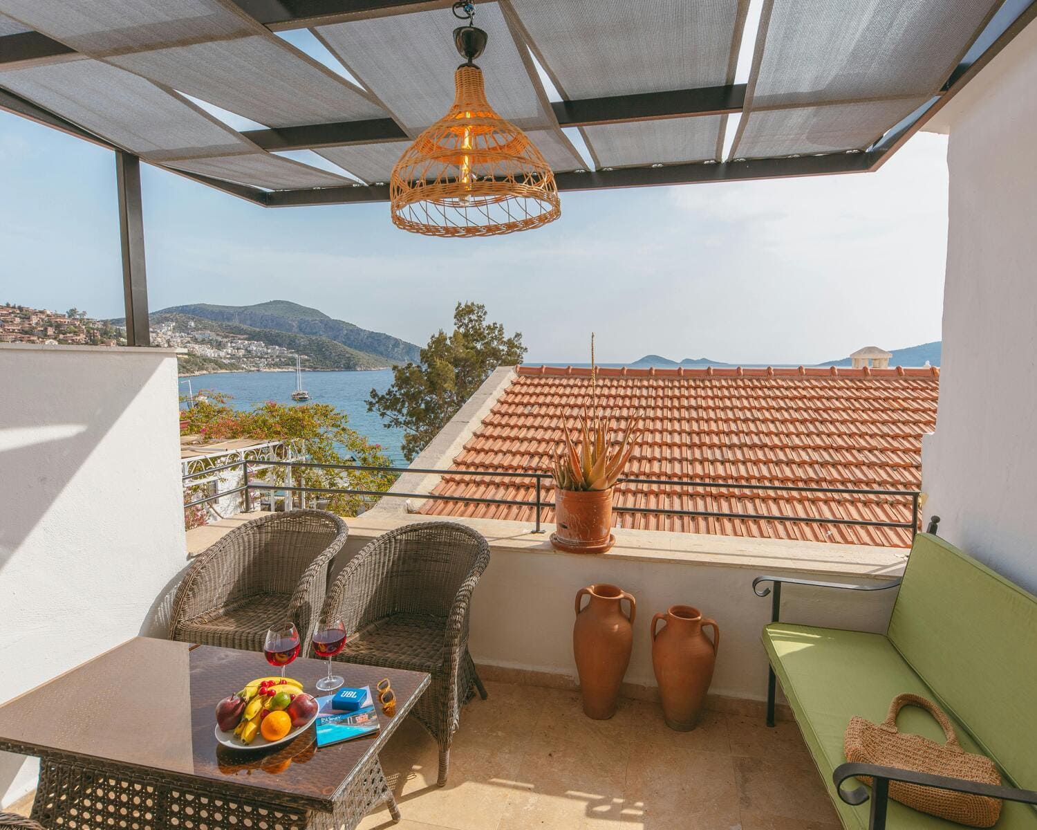 An outdoor dining area on a terrace with wicker chairs and a woven pendant light, overlooking a serene mountain and sea view, creating a perfect setting for relaxation.